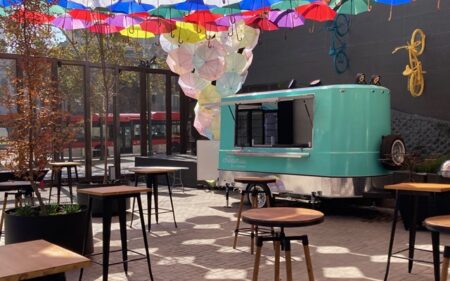 Decenas de paraguas multicolores cubren una terraza en el amplio espacio de la entrada al recinto, con un foodtrack de crepería.